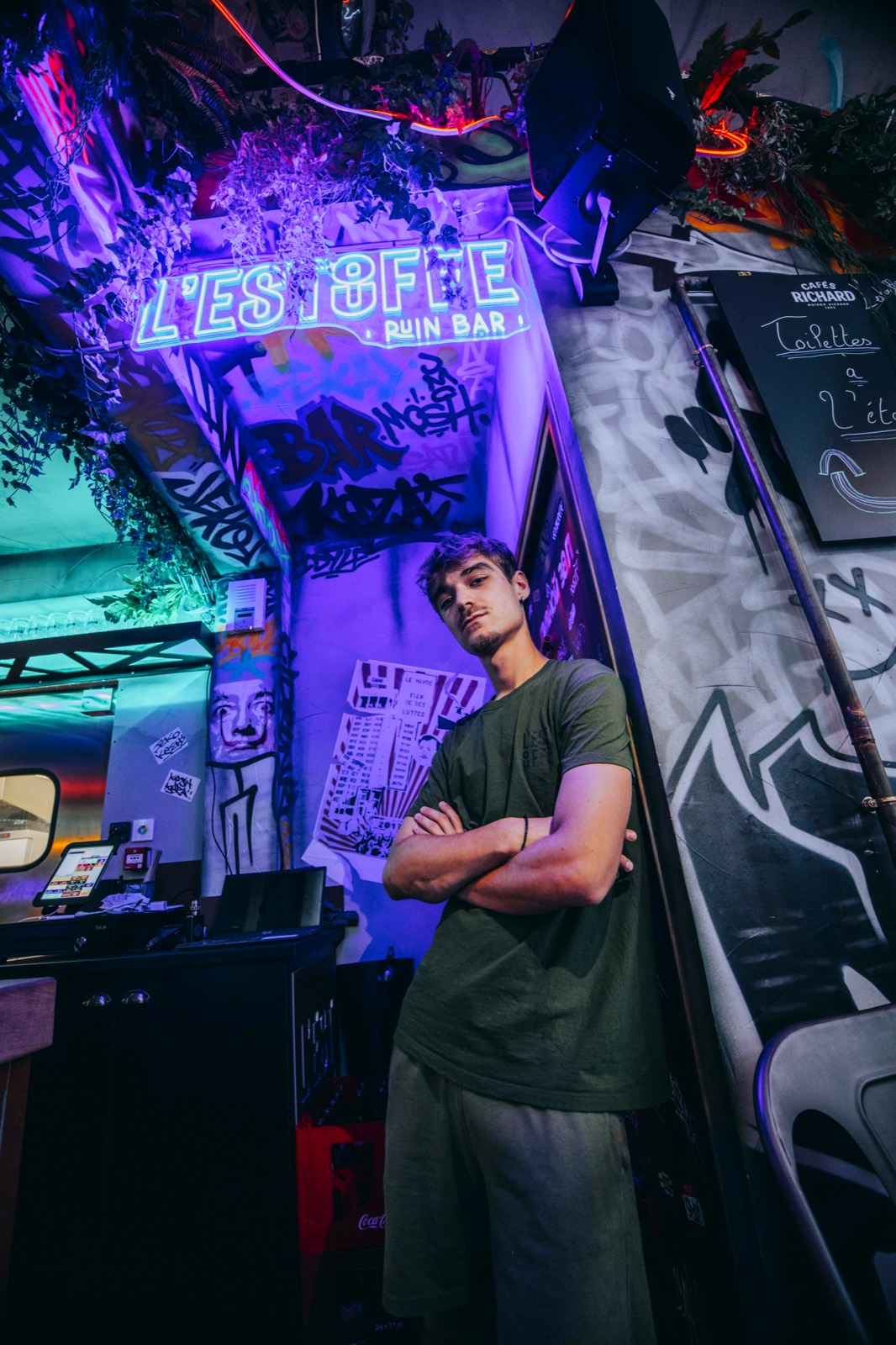 Homme posant devant l'enseigne néon du bar L'Estouffe