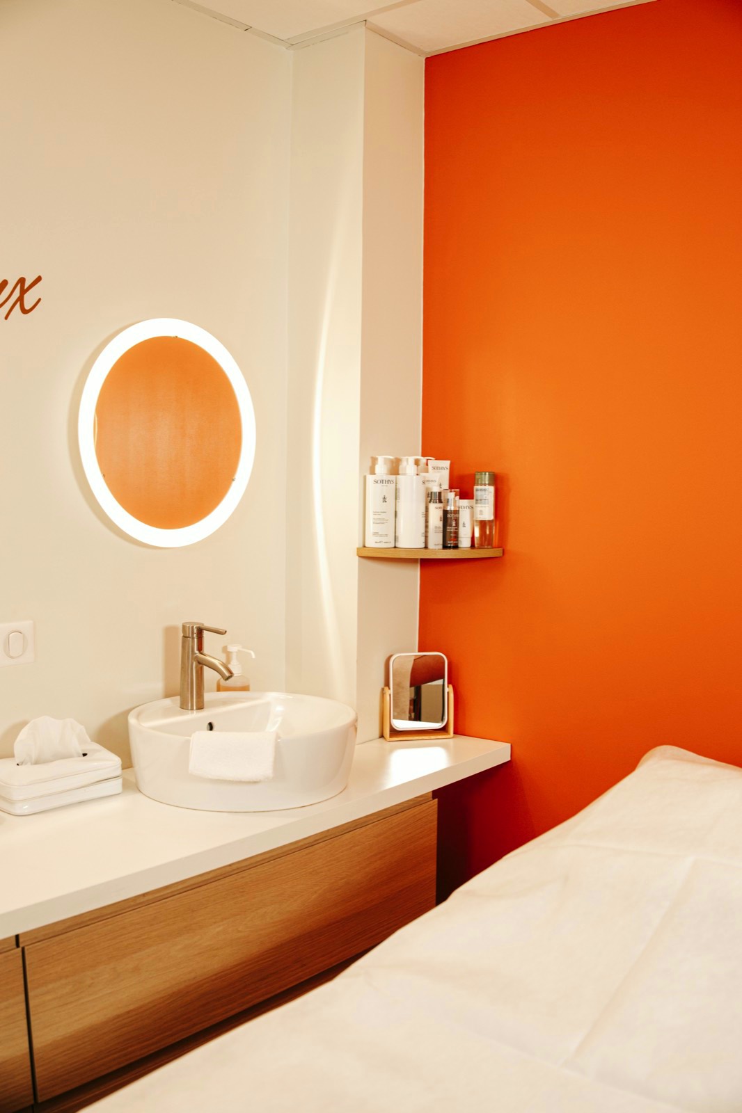 Cabine de soin : mur orange, miroir lumineux et table de massage