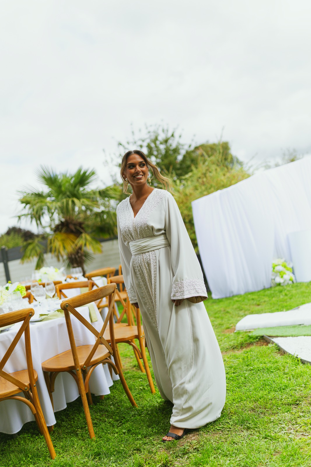 Invitée en caftan clair passant devant les tables dressées