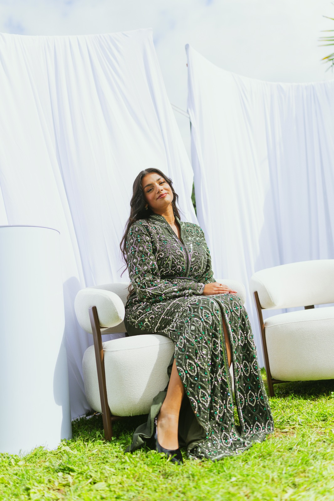 Portrait assis dans un fauteuil blanc, devant les tentures du décor